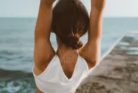 Woman practicing mindful wellness by the sea with arms raised