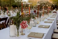 Wedding reception table styled with colorful flowers, orange taper candles, white linens and neutral place settings.