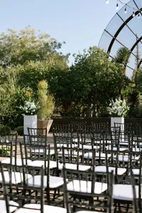 Outdoor wedding ceremony setup with black chairs, white floral arrangements and lush desert garden landscaping.