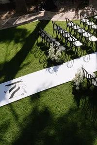 Modern outdoor wedding ceremony with black chairs, white floral arrangements and a custom white aisle runner.