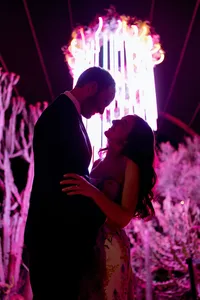 Newlywed couple embracing beneath a dramatic pink illuminated installation at their wedding reception.