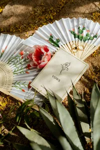 Wedding vow book, gold wedding rings and hand-painted floral fans styled with flowers and desert greenery.