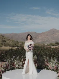 Bride holding a colorful bouquet in front of desert landscaping and Arizona mountain views.