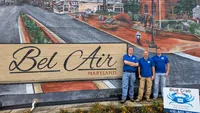Blue Crab Fence & Home owners Brian, Jim, and Brent stand with their yard sign in front of a painted Bel Air Maryland brick wall mural.