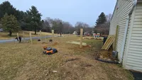 A worker rolling out and securing black wire mesh to a newly built line of wooden posts for a secure farm-style fence in Maryland.