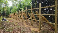 The completed structural framing of a tall wood privacy fence with stacks of premium wooden pickets staged and ready for installation in Maryland.
