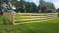 A custom 3-rail wood farm fence featuring wire mesh backing to secure an open, tree-lined Maryland yard.