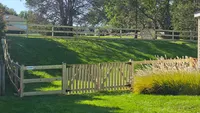 A classic wood 3-rail farm fence following the contour of a grassy residential hill in the Baltimore Metro region.