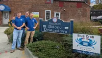 Blue Crab Fence & Home owners Jim, Brent, and Brian pose with their yard sign in front of the Historic Reisterstown welcome sign.