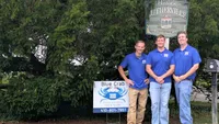 Blue Crab Fence & Home owners Jim, Brent, and Brian pose with their company yard sign in front of the Historic Lutherville welcome sign.