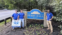Blue Crab Fence & Home owners Jim, Brent, and Brian pose with their company sign in front of the Perry Hall welcome sign.
