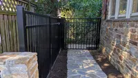 A custom black aluminum fence and matching walk gate installed across a flagstone pathway next to a stone house in Towson.