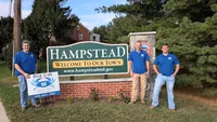 Blue Crab Fence & Home owners Jim, Brent, and Brian pose with their yard sign next to the Hampstead town welcome sign.