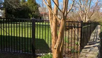 Black flat-top aluminum fence installed alongside a natural stone wall in a Towson, MD residential yard by Blue Crab Fence & Home.