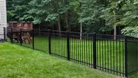 Black flat-top aluminum fence installed along a green residential backyard and wooded property line in Maryland by Blue Crab Fence & Home.