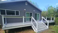 A custom built gray composite deck featuring clean white railings, black aluminum balusters, and a wide staircase for a Maryland home.