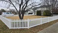 A classic white vinyl spaced picket fence enclosing a large, open front yard with a mature tree for a residential property in Maryland.