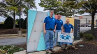 Blue Crab Fence & Home owners Jim, Brent, and Brian stand with their yard sign in front of the main entrance sign for The Avenue at White Marsh.