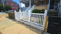 A decorative white vinyl scalloped picket fence featuring French Gothic posts, enclosing a front patio space along a city sidewalk in the Baltimore Metro area.