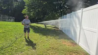 Blue Crab Fence & Home Jim Gangler uses a pressure washer to thoroughly clean a newly installed white vinyl privacy fence in Maryland.