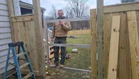 Blue Crab Fence & Home owner Brian Butterhoff test-fits a heavy-duty custom metal gate frame into a newly built wood privacy fence to ensure perfect alignment in Maryland.