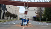 Blue Crab Fence & Home owners Jim, Brent, and Brian pose with their branded yard sign directly underneath the Towson Town Center entrance sign.