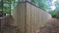 A tall, custom wood privacy fence corner installed in a wooded residential backyard in Maryland.