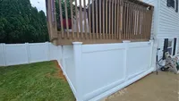 A custom white vinyl privacy fence installed neatly beneath a raised wooden deck, enclosing the lower yard of a Maryland home.
