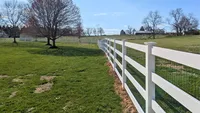 A heavy-duty white vinyl 3-rail farm fence backed with green wire mesh, enclosing a large open pasture property in Marriottsville.