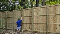 Blue Crab Fence & Home owner Brent Donahue inspects the interior framing and checks the heavy-duty wooden posts of a tall custom wood privacy fence in Maryland.