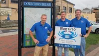 Blue Crab Fence & Home owners Jim, Brent, and Brian stand next to a Downtown Bel Air directory map with their branded yard sign.