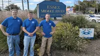 Blue Crab Fence & Home owners Brian, Brent, and Jim pose with their branded yard sign in front of the Essex Middle River Gateway to the Chesapeake sign.