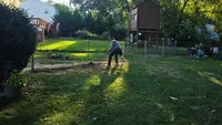 A worker clearing brush, leveling dirt, and prepping the property line prior to a new custom fence installation in the Baltimore region.