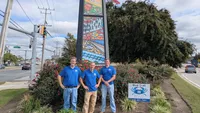 Blue Crab Fence & Home owners Jim, Brent, and Brian stand with their company yard sign in front of the Essex community history mural.