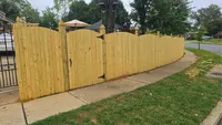 A premium wood privacy fence curving gently along a residential sidewalk and driveway in the Baltimore Metro area.