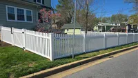 A white vinyl spaced picket fence with a matching gate, securing the front yard of a home with a blooming dogwood tree in Halethorpe.