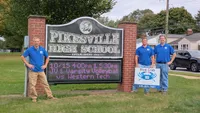 Blue Crab Fence & Home owners Jim, Brent, and Brian stand with their yard sign next to the Pikesville High School sign.