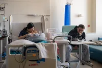 Parents rest beside their newborn in a hospital room with the bassinet between them.