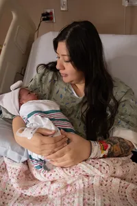 Mother holds her newborn while lying in the hospital bed.