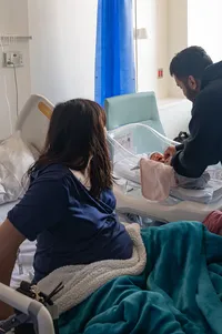 Dad helps his newborn baby while Mom watches from the hospital bed.