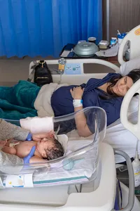 Mom watches her newborn girl as the doctor reaches to pick her up.