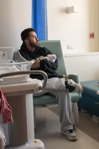 Dad sits and holds his newborn in his arms as he looks out the hospital window.