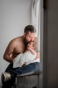 Dad kisses his baby while sitting on the windowsill.
