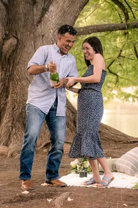 An engaged couple popping champagne and laughing as it gets all over them.