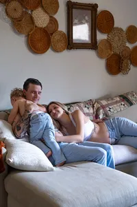 Expecting parents relax on the sofa as their toddler hugs his dad.