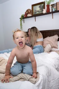Expecting parents kissing in the background as their toddler yells into the camera.