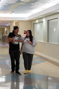 Parents walking down the hospital hallway with their newborn baby in arms.