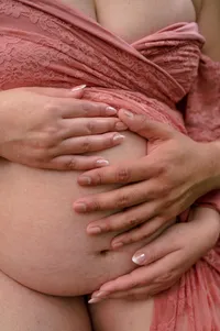 Close-up of two people resting their hands together on a pregnant belly.