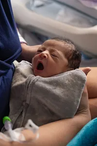 Newborn baby yawns in her mother’s arms.