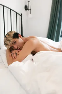 Queer man lays on the bed, looking at the camera.